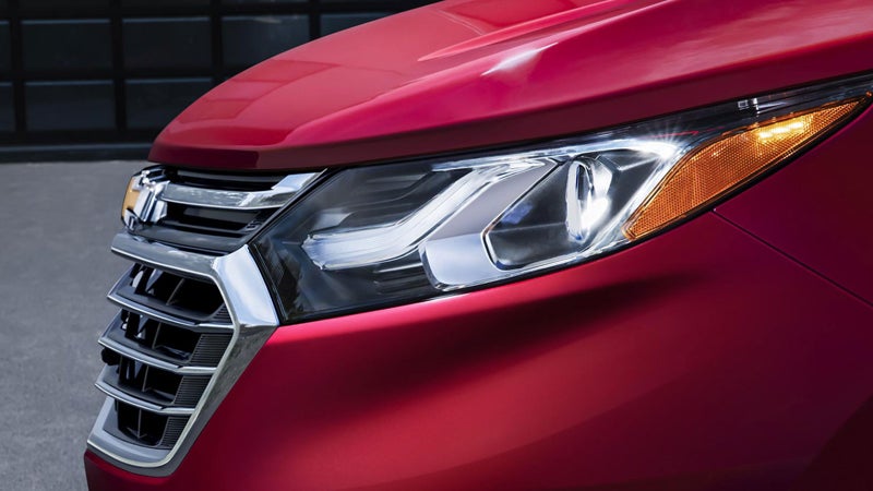 Close-up of a red Chevrolet Equinox headlamp, showcasing its sharp, angular design with a bright, modern light pattern