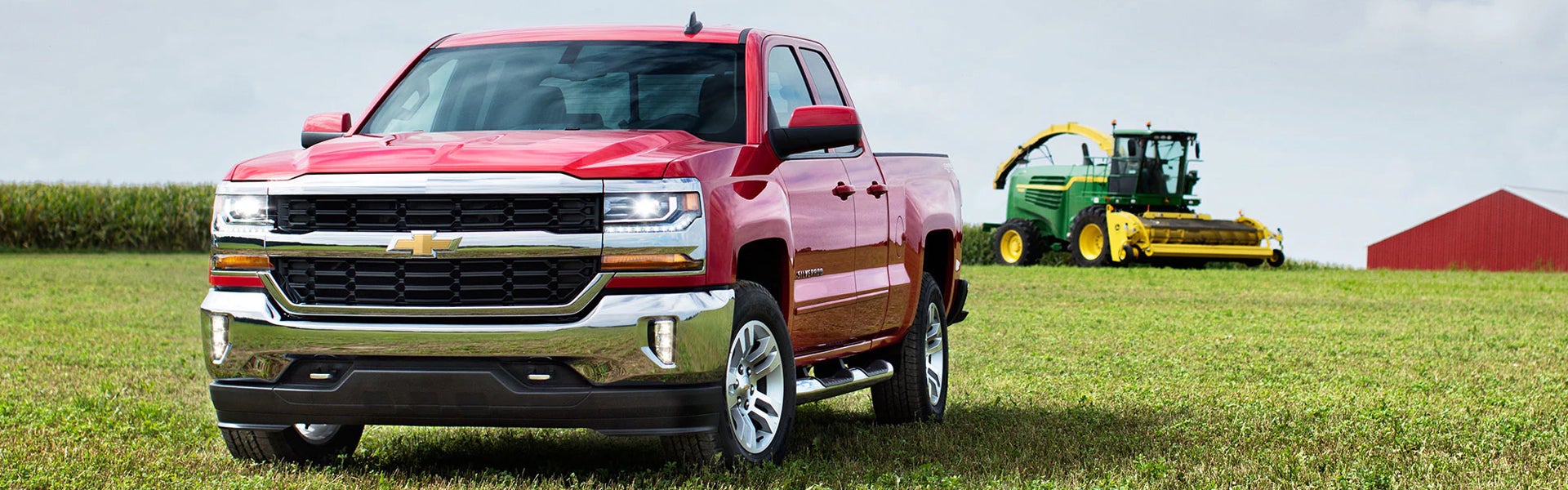 red Chevrolet Silverado 1500 pickup truck is parked on a grassy field with a harvester in the background