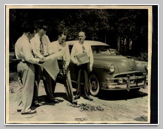 Vintage black and white photo of people gathered by a car.