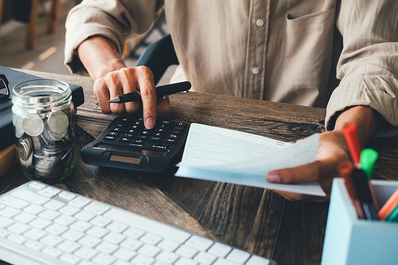Man using calculator with paper in hand and coins on table