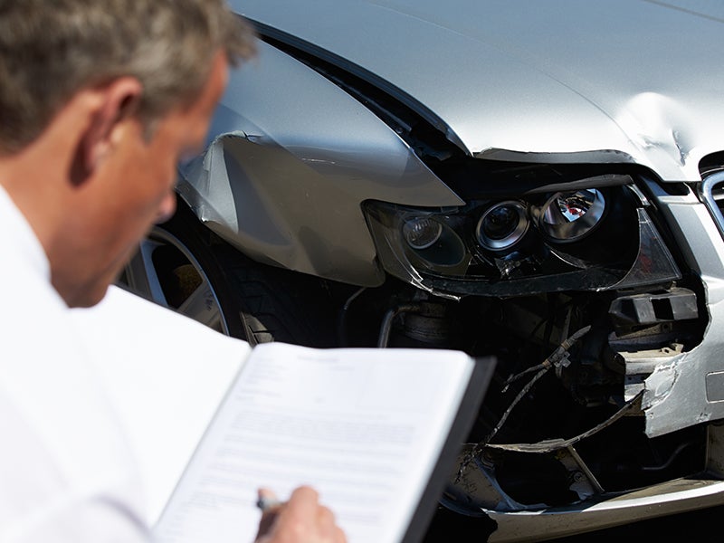 Man inspecting documents near a damaged car.