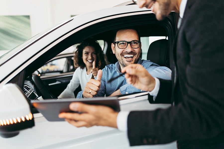 Happy couple in car giving thumbs up to salesman